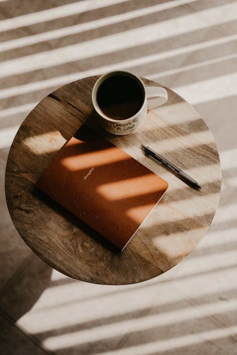 A journal, pen, and warm cup of coffee on a sunlit wooden table